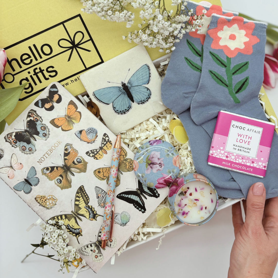 A gift set box containing vintage-style items including floral-patterned items, a candle, socks, a notebook, and a pen.