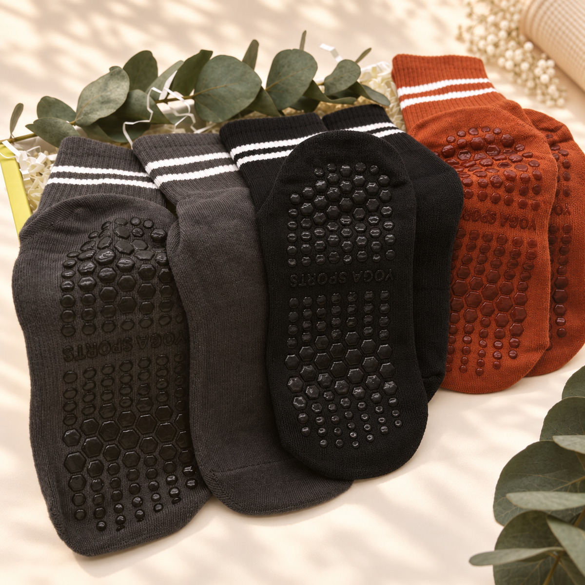 Four pairs of grip socks arranged in a fan shape, showing the textured non-slip soles. The socks come in black, dark gray, white-striped black, and rust-orange colors.