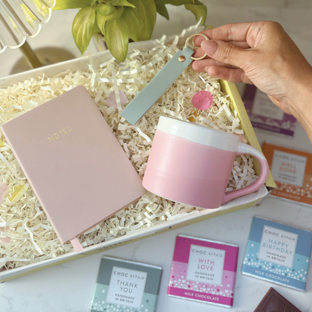 Pink mug, keyring and notebook in a gift box with chocolates.
