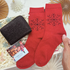 Red socks with snowflake design held by a hand, next to a black glittery purse and chocolate on a decorative giftbox.