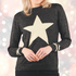 Christmas jumper in black with gold star. A woman smiling and wearing a black glitter wool blend jumper with a gold star and stripe print, long sleeves, and a round neck.