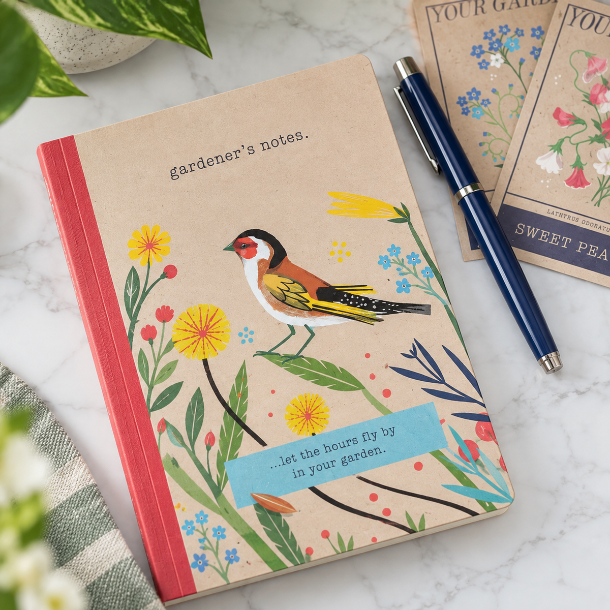 A decorative hardcover notebook with a bird and floral illustration on the cover, placed on a marble surface with a blue pen and matching cards nearby.