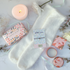 Set of beauty products including a bar of soap, candle, bracelet and fluffy socks on a soft surface with flowers.