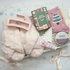 Gift set with fluffy pink item, Christmas-themed box, pink socks with tree design, and skincare products on a light background.