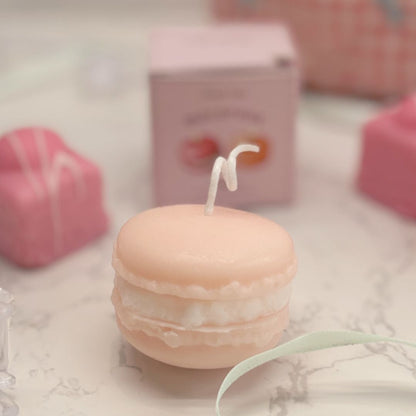 Macaron-shaped candle with a small candle on top, surrounded by pink and white decorative items.