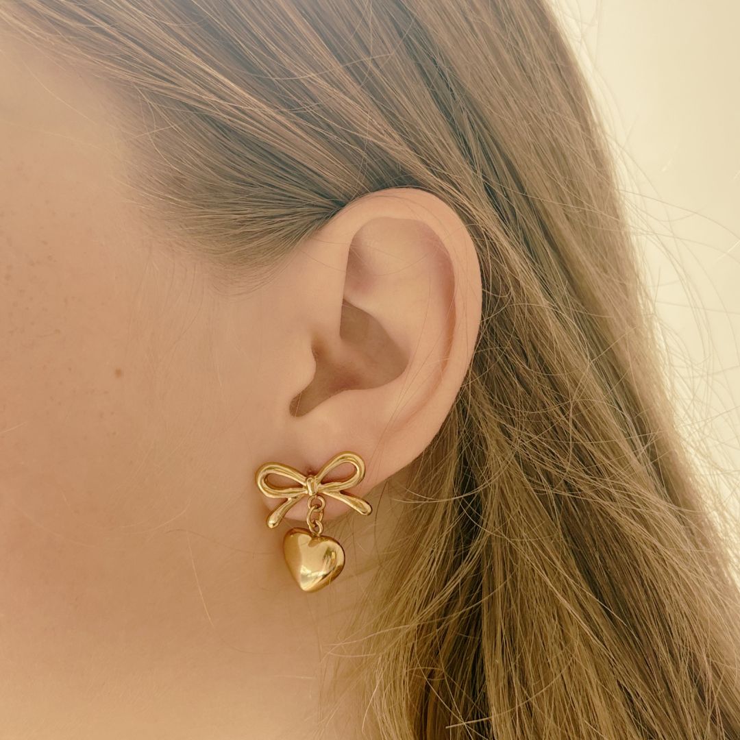 Gold bow and heart earring worn by a person with blonde hair.