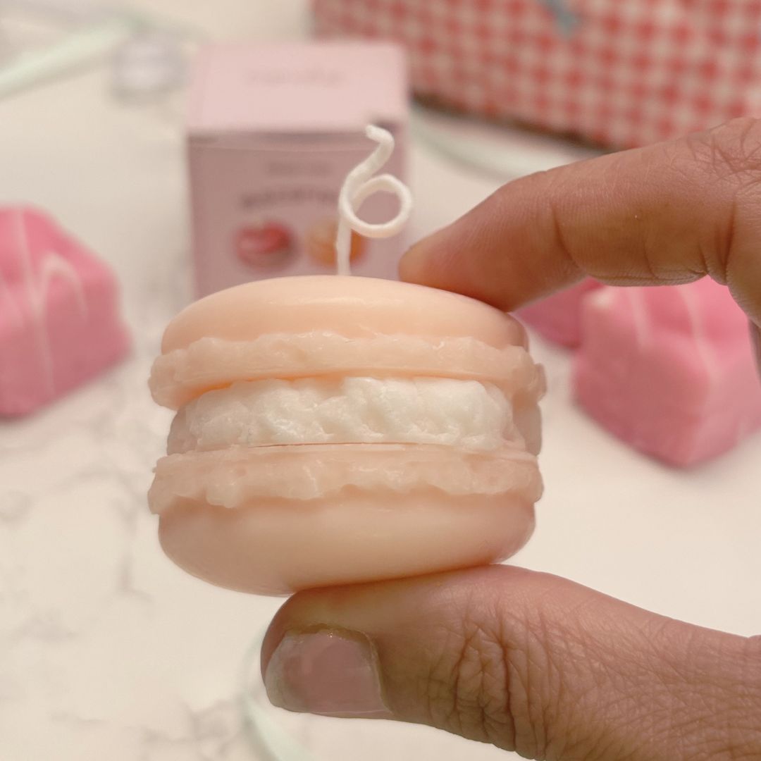 Hand holding a small pink and white macaron-shaped product with a blurred background