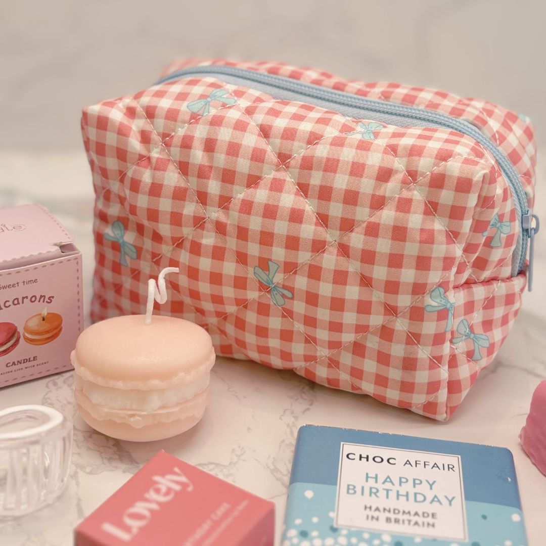 Pink gingham makeup bag with a candle and small books on a light surface