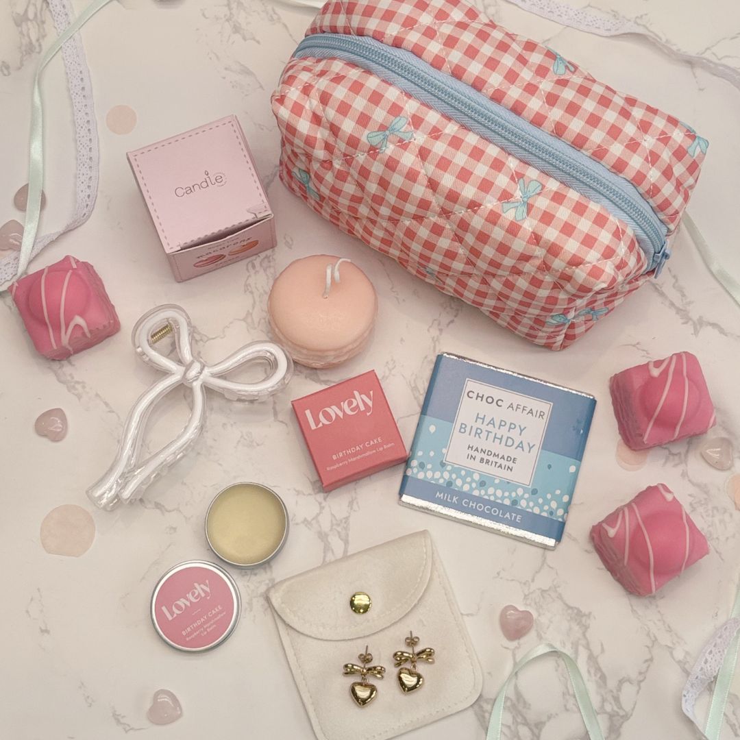 Assorted small items including a gingham make up bag, candles, and chocolate on a patterned surface.