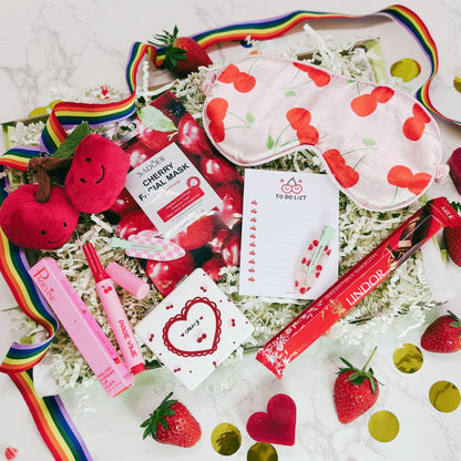 Assorted cherry-themed products including a mask, lip balm, and chocolate on a white background with strawberries and rainbow elements.