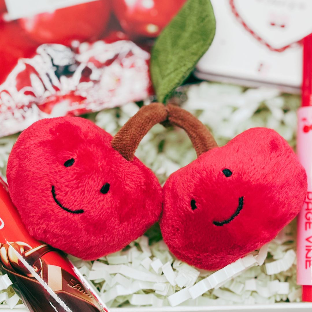 Two red plush cherries with smiling faces on a white surface.