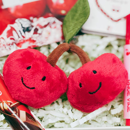 Two red plush cherries with smiling faces on a white surface.