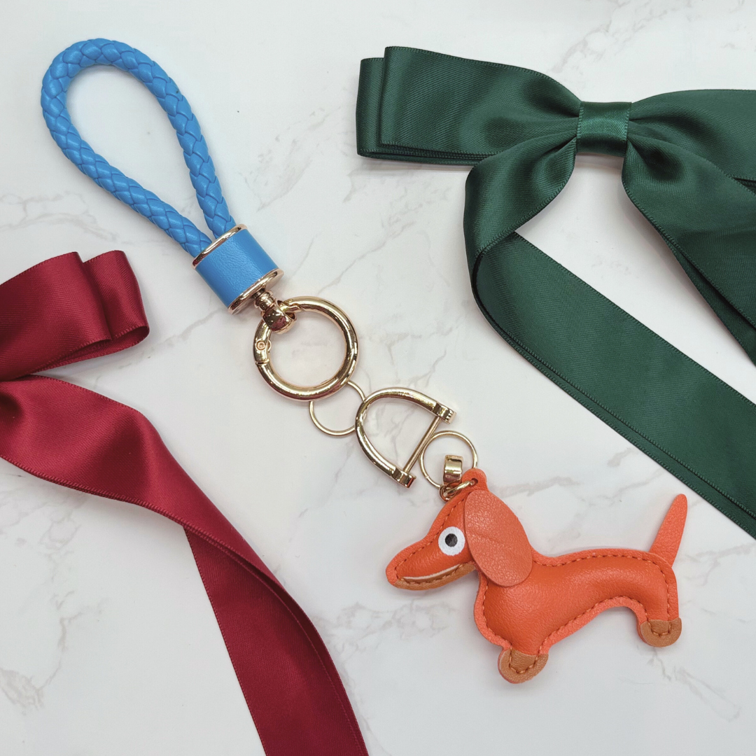 Dog Keyring. Orange dachshund-shaped keychain with blue and green ribbons on a white background