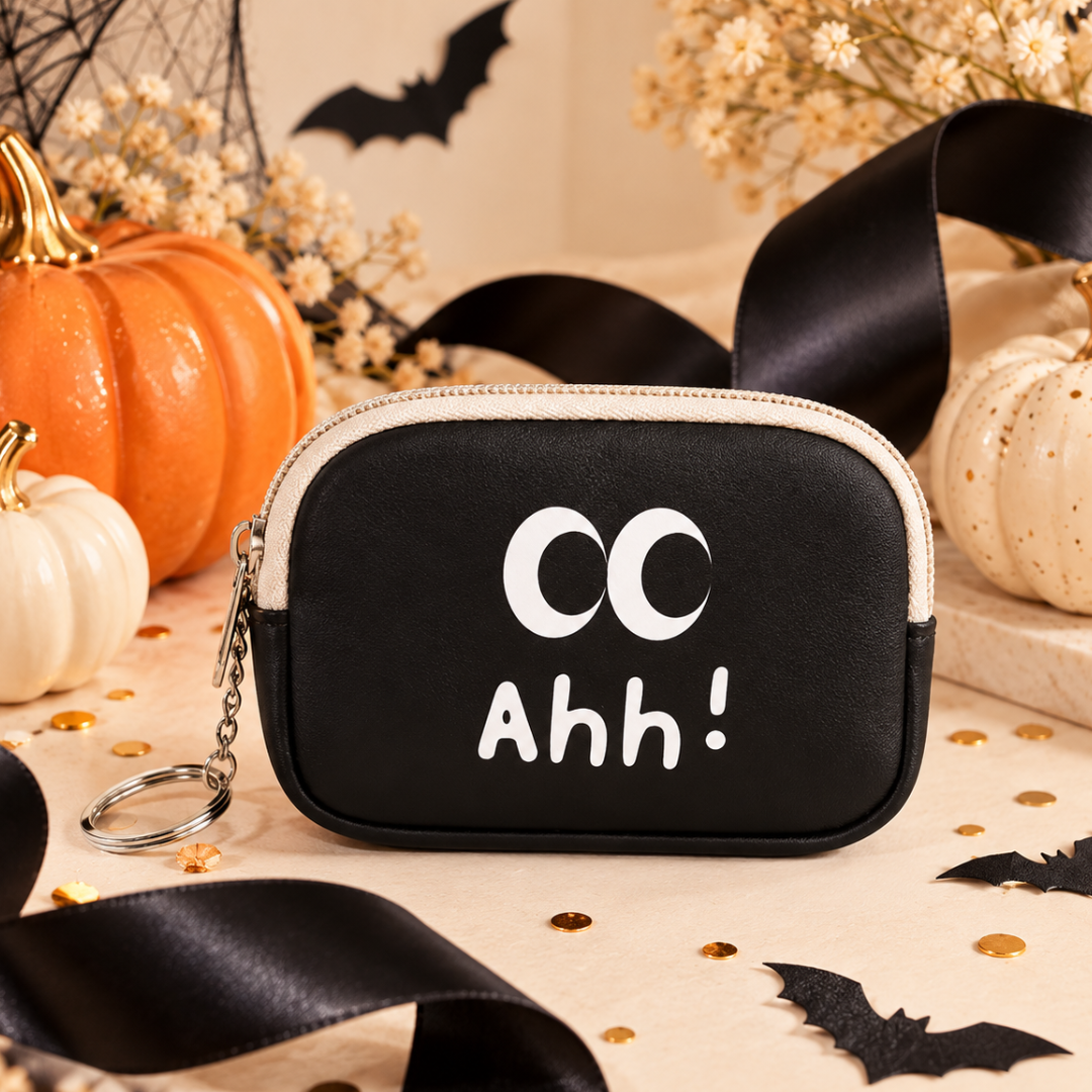 A black faux-leather coin purse with a cream zipper trim and a keychain ring, featuring the white printed text &