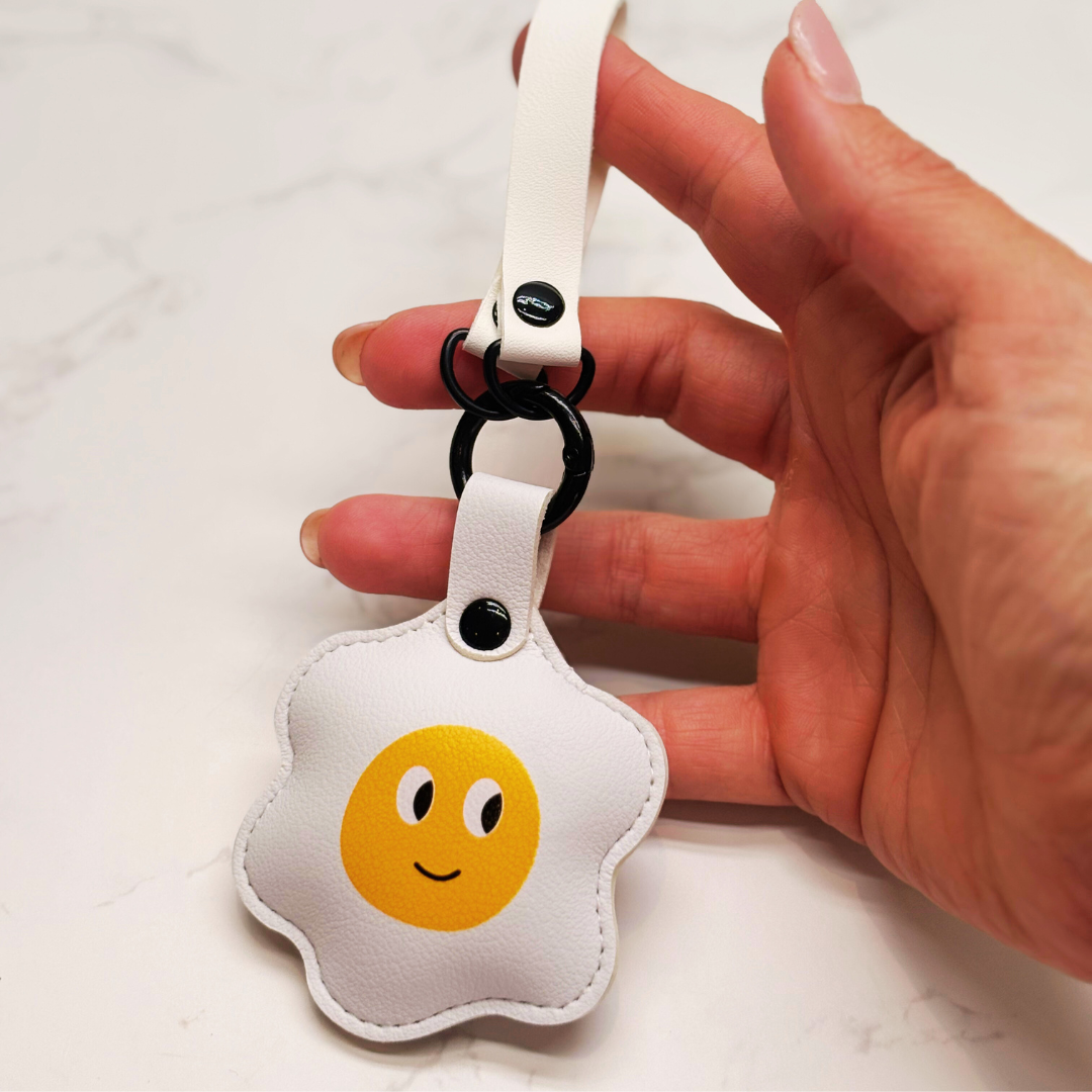 Fried egg cute keyring. Hand holding a keychain with a smiley face design on a white background