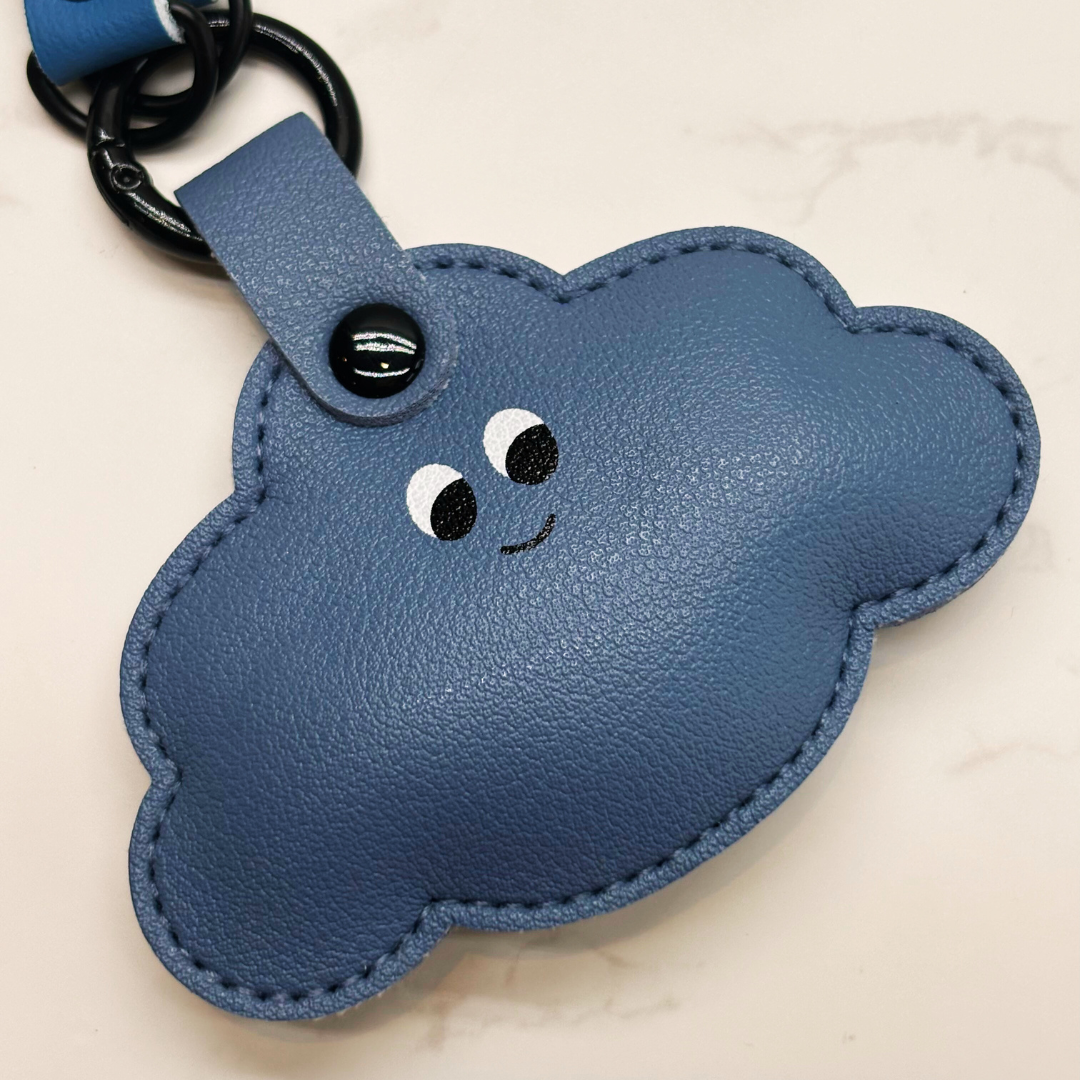 Blue cloud-shaped keychain with a smiley face on a beige background
