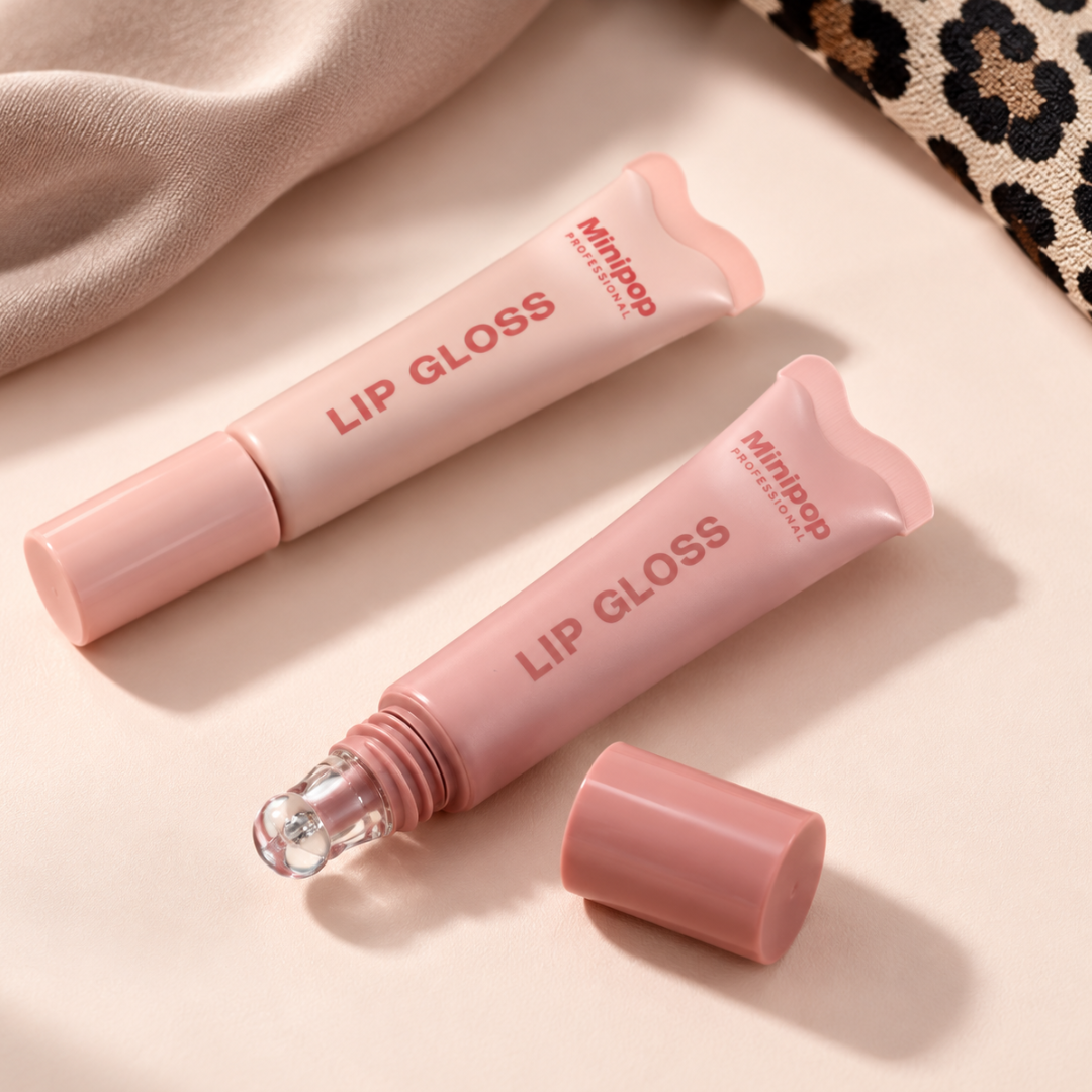 Two pink lip gloss tubes from Minijop on a light beige surface, one upright and one lying down with its cap removed to show the clear roller ball, styled with a beige fabric and a leopard print corner.