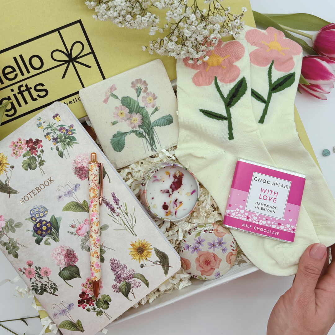 A gift set containing a variety of floral-themed items including socks, a notebook, a candle, a coaster, and a pen, all displayed in a box with a &