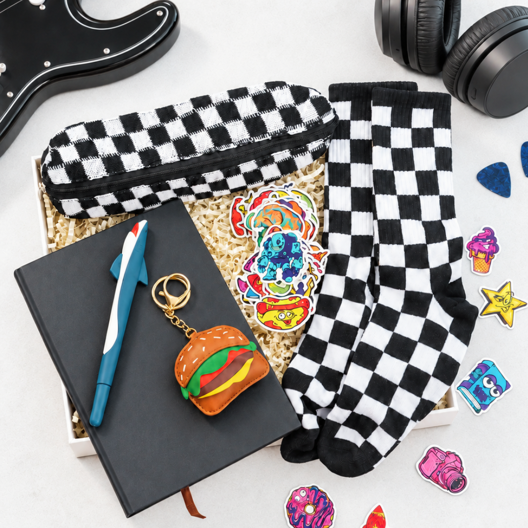 A flat-lay gift set featuring black and white checkered socks and a matching zippered pouch, displayed with a black notebook, blue pen, hamburger keychain, and colorful enamel pins on a white background.