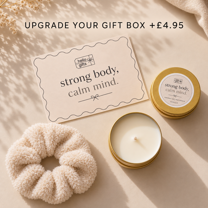 A styled gift set on a warm beige surface with soft shadows. The set includes a cream scrunchie, a cream gift card reading &