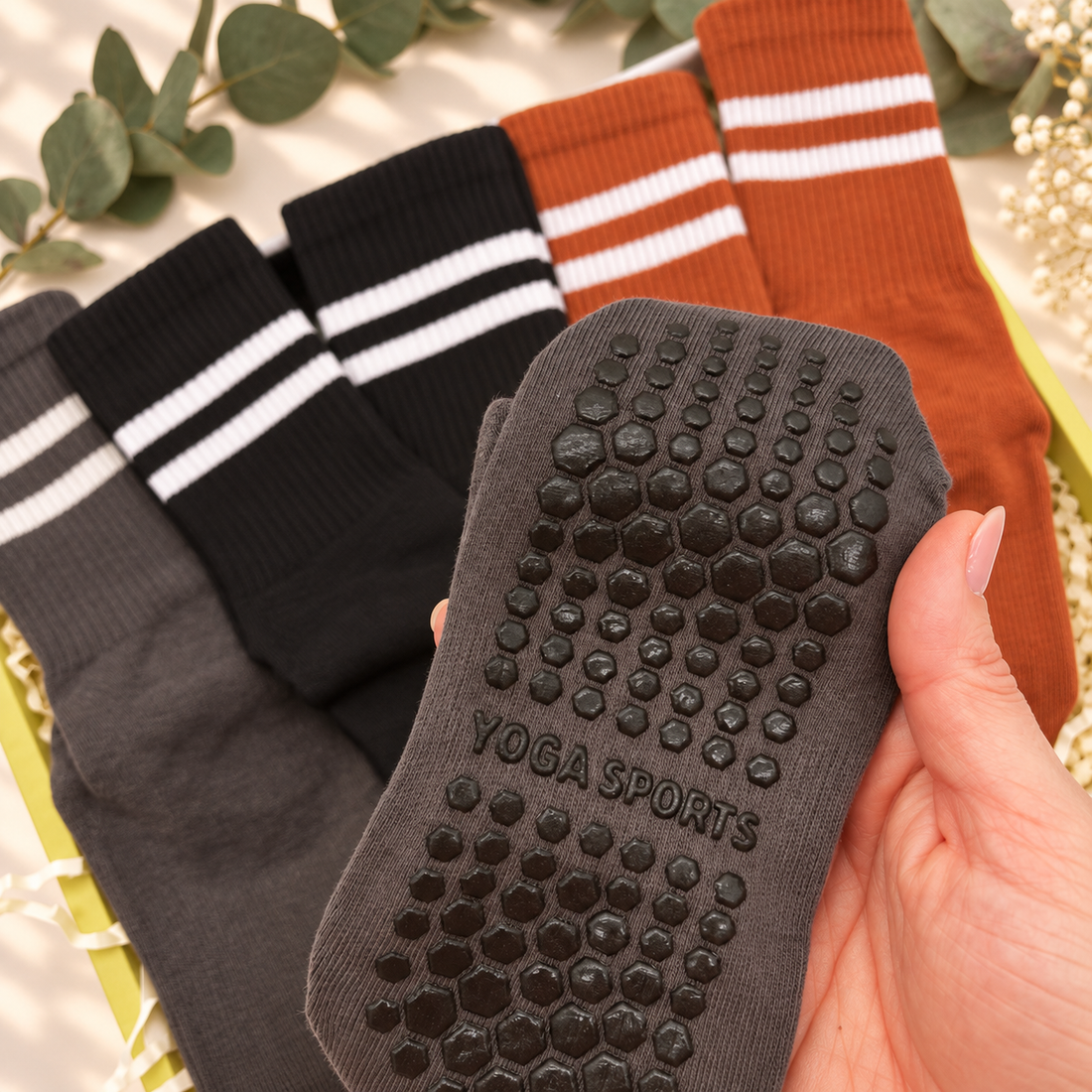 A hand holds a dark gray yoga sock with a raised hexagonal grip pad and the words &
