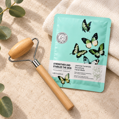A teal facial mask pouch labeled Jasmine Ceramide Nourishing Facial Mask lies on a beige textured surface beside a wooden roller tool and a folded cream towel, with eucalyptus leaves in the corner.