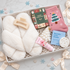 A curated gift box set containing a fluffy white slipper, a pink Christmas-themed sock, a green &