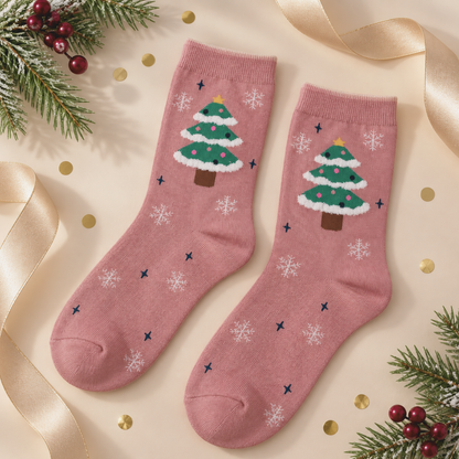 A pair of dusty rose crew socks with a festive Christmas tree and snowflake pattern, styled on a beige background with gold ribbons, pine branches, and red berries.