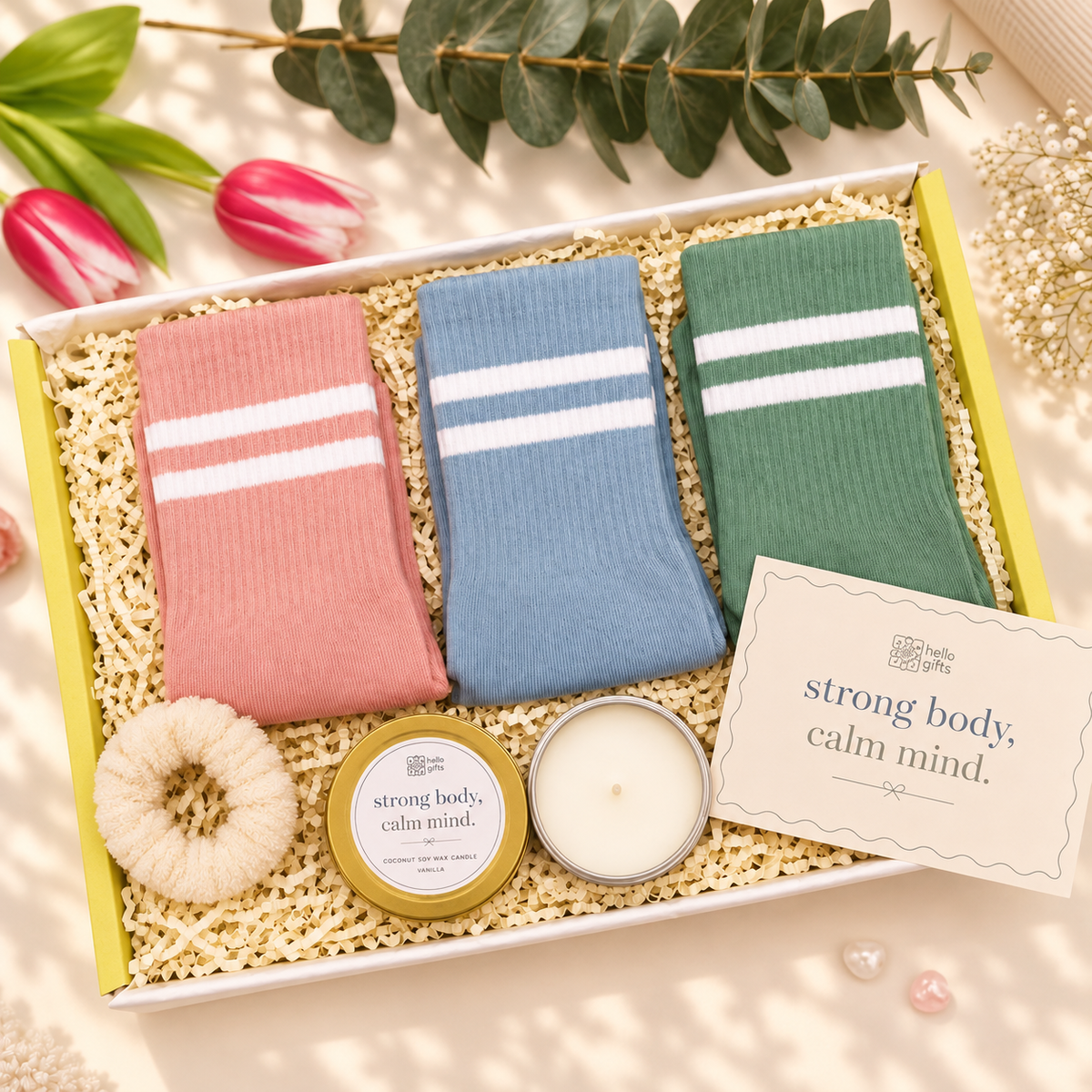 A gift box set containing three pairs of striped socks in pink, blue, and green, a cream scrunchie, a small tin candle, a white candle, and a card that reads &