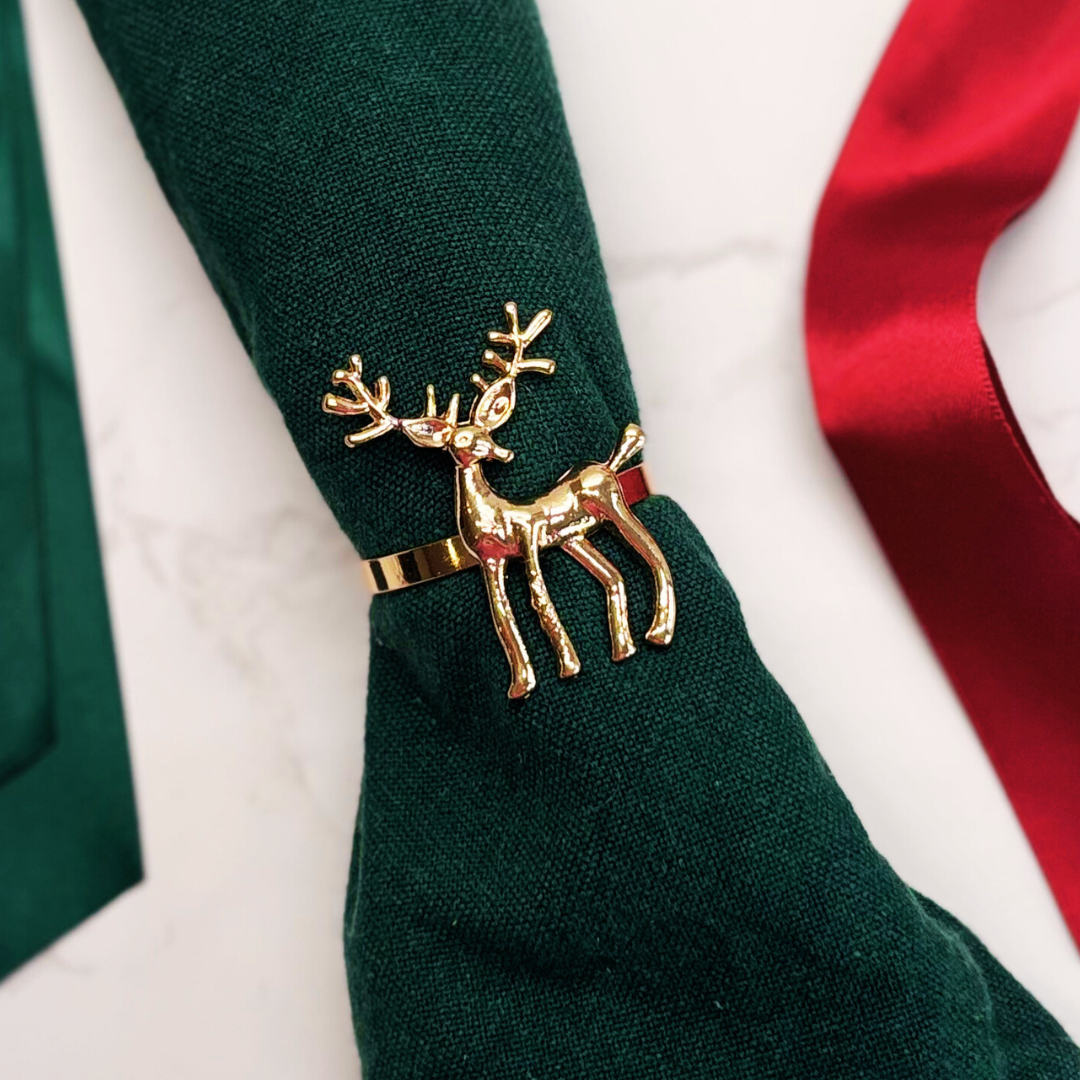 Napkin rings, snowflake or reindeer design. Gold reindeer napkin ring on a green napkin with a red ribbon in the background.