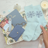 Light blue socks with snowflake design held by a hand, next to a notebook, wallet, and gift box on a decorative surface.