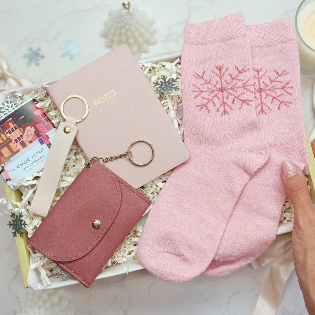 Pink wallet, keychain, and socks with snowflake design on a decorative surface.