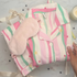 Folded pajama set with pink and green stripes, fluffy pink eye mask on a lemon yellow gift box. 
