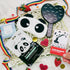 Collection of panda-themed products including face masks, a heart-shaped mirror, and stationery items on a white surface with strawberries and ribbons.