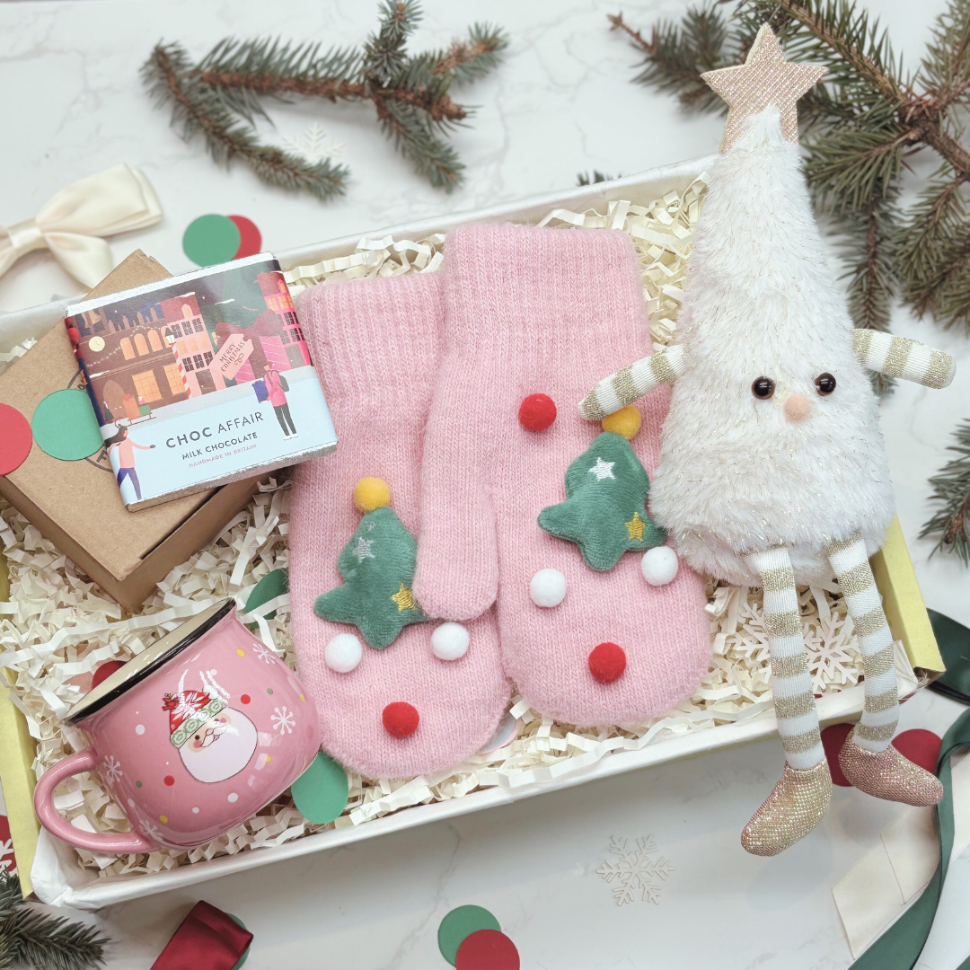 Christmas Eve Box. Gift set with pink mittens, mug, and decorative figure on a white surface with Christmas decorations.
