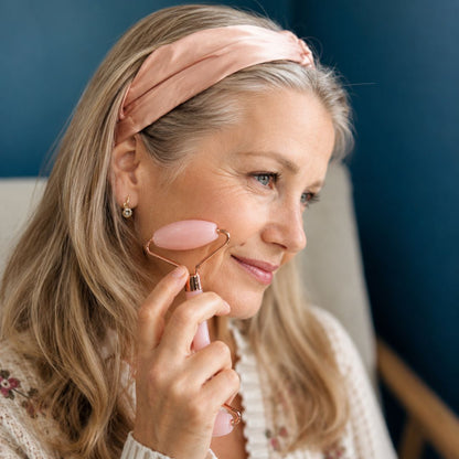 Woman using a pink facial roller on her face with a blue wall background