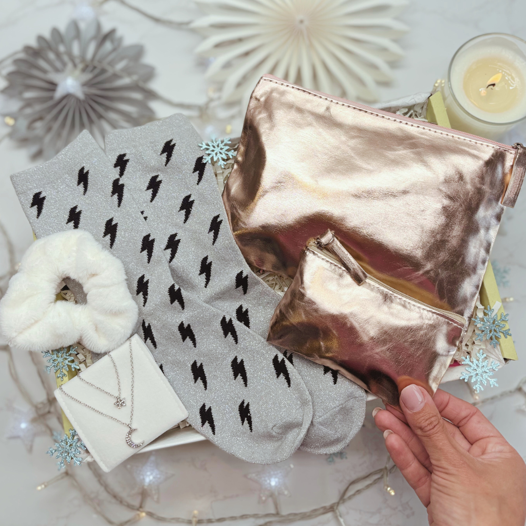 Hand holding a metallic pouch with gray socks featuring black lightning bolts on a decorative surface.