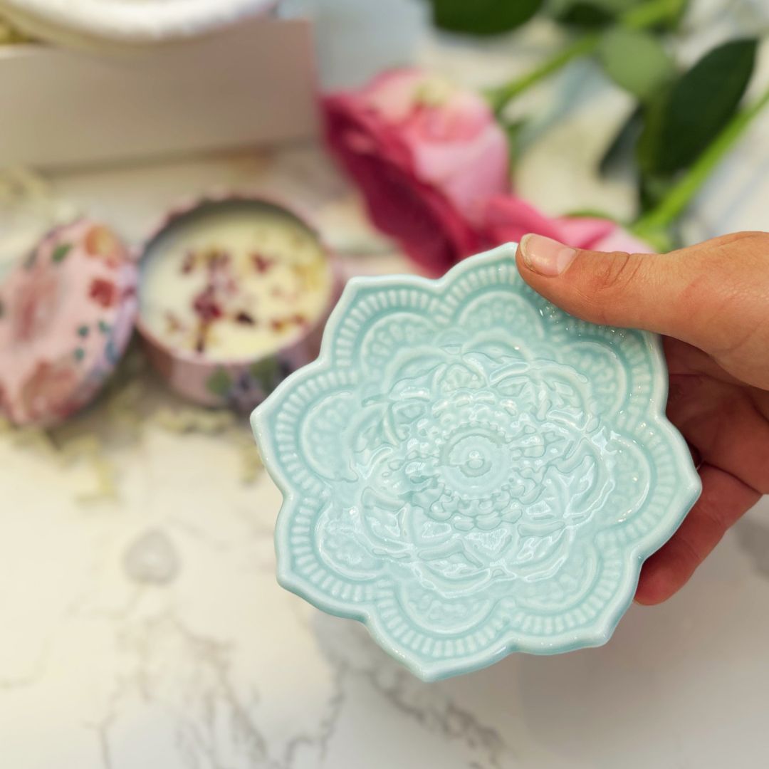 Hand holding a light blue ceramic dish with intricate patterns on a blurred background.
