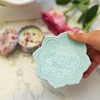 Hand holding a light blue ceramic dish with intricate patterns on a blurred background.