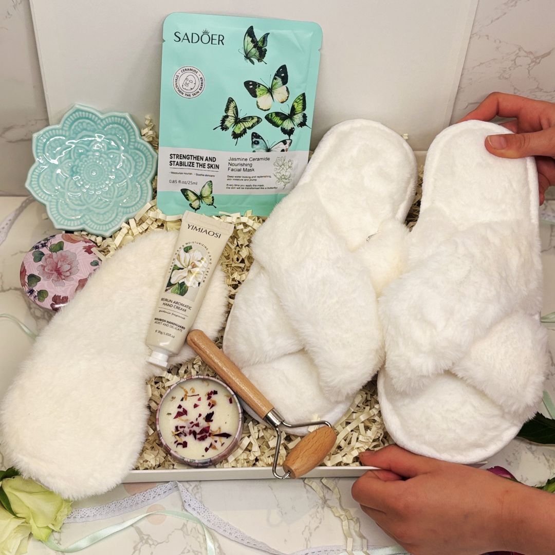 White fluffy slippers with a giftbox of skincare products and skin roller on a marble surface.