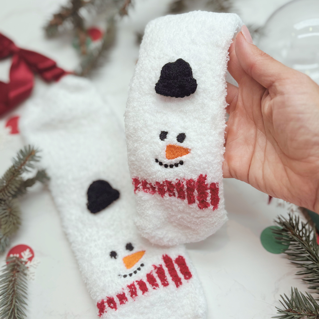Hand holding a snowman-themed sock which comes in a clear bauble with Christmas decorations in the background