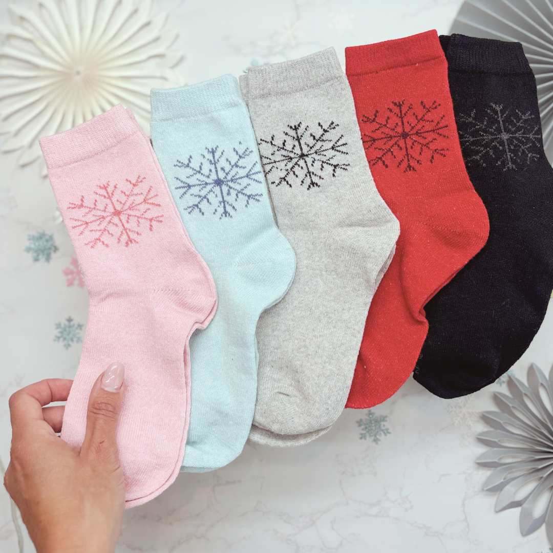 Five pairs of socks in pink, blue, gray, red, and black with snowflake designs on a decorative background.