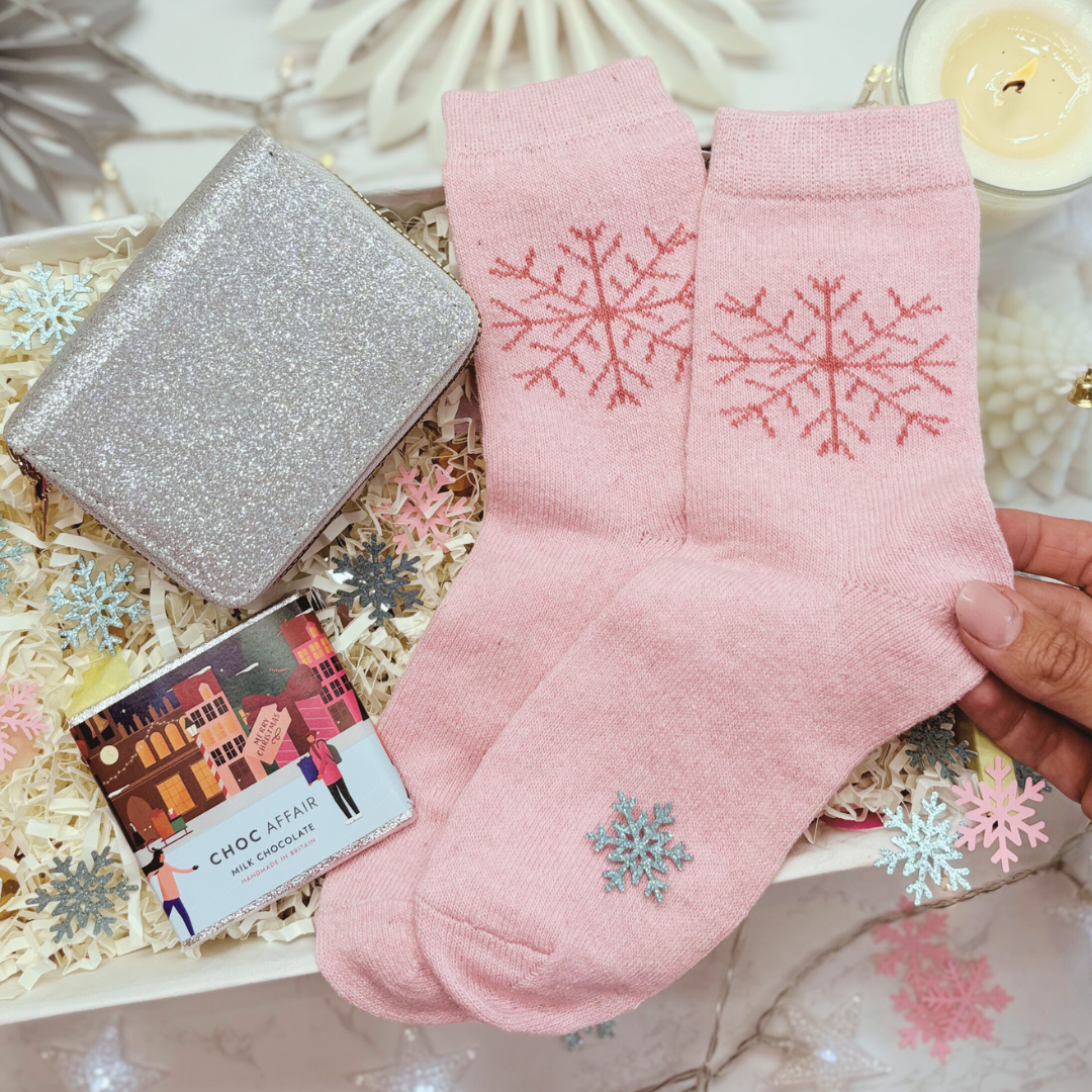 Pink socks with snowflake designs, glitter purse, held over a gift box with chocolates and a card.