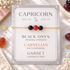 A gold chain bracelet with three beads (two black onyx, one red carnelian) displayed on a branded backing card that reads &