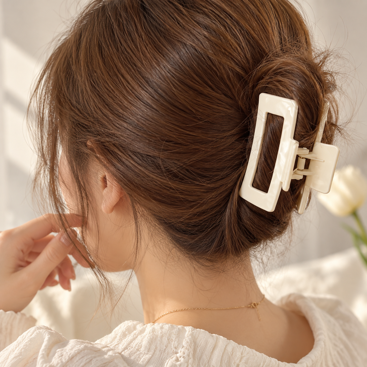A woman shown from the back wearing a large cream-colored rectangular claw hair clip holding her brown hair in a low bun.