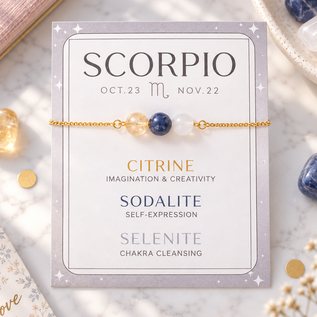 A Scorpio-themed crystal bracelet displayed on its printed card, featuring citrine, sodalite, and selenite beads on a delicate gold chain, set against a marble background with crystals.