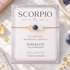 A Scorpio-themed crystal bracelet displayed on its printed card, featuring citrine, sodalite, and selenite beads on a delicate gold chain, set against a marble background with crystals.