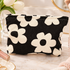 A black corduroy cosmetic pouch with a large cream floral pattern, styled on a marble surface with beauty props and flowers in the background.