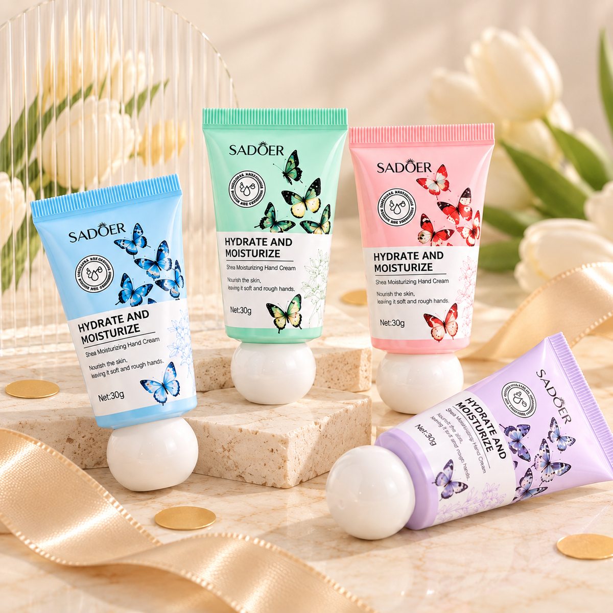 Four Sadoer Hydrate and Moisturize hand cream tubes in blue, mint green, pink, and lavender, arranged on decorative blocks with tulips and gold coins in a styled studio setting.