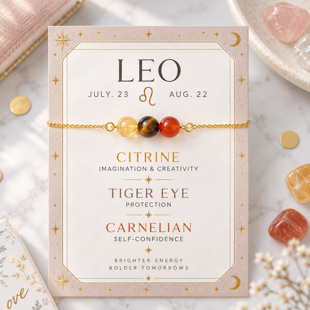 A gold chain bracelet with three beads (citrine, tiger eye, and carnelian) displayed on a decorative card featuring astrological details for Leo. The card is styled on a marble surface with crystals and gold coins.